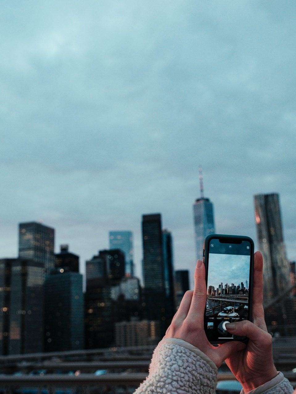 A person taking photos of the NYC skyline from the Brooklyn Bridge