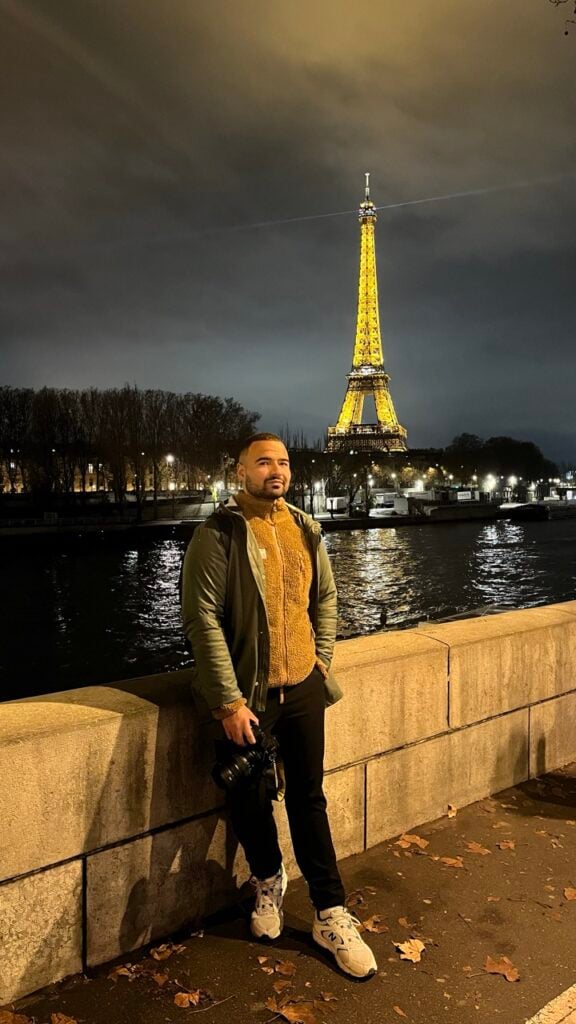 A man standing outside the Eiffel Tower at night